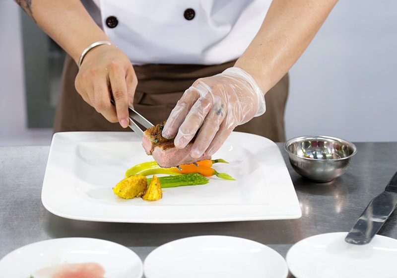 A professional chef putting together a dish on a white plate.