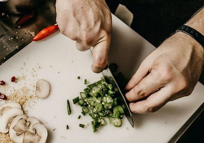 A person cutting vegetables on a white surface.